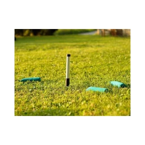 Ein schwarz-weißer Markierstab steckt in einer grünen Wiese. Darum herum liegen mehrere grüne Dummybeutel.